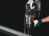 A person wearing gloves is using a cordless hammer drill to drill into a metal beam. Produktbild-Vorschau