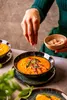 A person is garnishing a bowl of soup with herbs and spices. Náhľad obrázku produktu