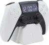 A white and black PlayStation controller shaped alarm clock sits on its white charging stand. Náhled obrázku produktu