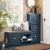 A blue shoe cabinet with a cushioned top, placed next to a window with plants and a door. Produktbild-Vorschau