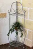 A metal corner shelf unit with a plant on it, placed in a corner against a stone wall. Podgląd zdjęcia produktu