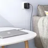 A laptop is charging on a table next to a sofa, with a wall charger plugged into an outlet. Produktbild-Vorschau