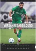A soccer player in a green jersey running with a soccer ball on a green field. Produktbild-Vorschau