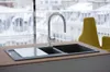 A modern kitchen sink with a faucet and a cutting board, with a blurred background of a city view in winter. Anteprima dell’immagine prodotto