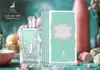 A perfume bottle and its box are displayed on a table with decorative elements like candy and flowers. Produktbild-Vorschau
