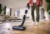 A person is using a cordless vacuum cleaner on a wooden floor in a well-lit living room. Náhľad obrázku produktu