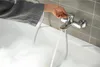 A person's hand is turning on a bathtub faucet, filling the tub with water and creating foam. Anteprima dell’immagine prodotto