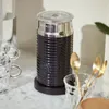 A Nespresso milk frother is shown on a marble countertop, along with glass cups and golden spoons. Náhľad obrázku produktu