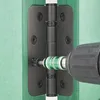 A close-up shot of a black door hinge being installed on a green door frame with a power drill and a SPAX screw. Náhled obrázku produktu