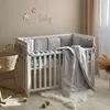 A white baby crib with gray bedding and a blanket inside, placed on a wooden floor with a small rug and wooden blocks. Anteprima dell’immagine prodotto
