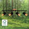 A black spotlight fixture with wooden accents is mounted on a black bar, set against a blurred background of a forest. Produktbild-Vorschau