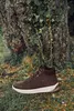 A brown high-top sneaker is placed on the grass in front of a large tree. Voir les images du produit