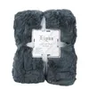 A folded dark gray plush throw blanket is presented on a white background, with a label attached. Produktbild-Vorschau