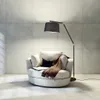 A modern floor lamp with a black fabric shade is positioned next to a comfortable white armchair in a room with tiled walls and floor. Náhled obrázku produktu