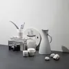 A still life arrangement of kitchenware and a camera on a dark surface against a white wall. Voir les images du produit