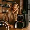 A woman smiling in a kitchen next to an air fryer. Produktbild-Vorschau