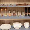Shelves in a cabinet displaying kitchenware, including spice grinders, plates, and bowls. Náhled obrázku produktu