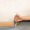 A hand is using a utility knife to cut carpet next to a wooden baseboard. Produktbild-Vorschau