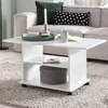 A white coffee table with storage is placed on a rug in a living room setting, with a sofa and pillows in the background. Voir les images du produit