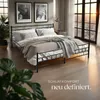A bedroom scene with a metal bed frame, bedding, and a large window with a sunset view. Náhled obrázku produktu