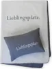 A folded blanket with a pillow on top, both featuring the same text. Produktbild-Vorschau