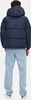 A person wearing a blue puffer jacket and light blue jeans, shown from the back. Produktbild-Vorschau