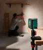 A man is using a laser level to measure and mark a wall while a laser level is clamped to a table in the foreground. Produktbild-Vorschau