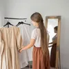 A woman is standing in front of a clothing rack with dresses, looking in a mirror. Produktbild-Vorschau