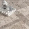 A close-up view of a round, beige shaggy rug with a white tray containing a white lantern, a gray candle, and a white apple. Anteprima dell’immagine prodotto