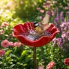 Lebhaft rote Glasvogeltränke auf Gartenstab, mit einem Vogel, der aktiv im Wasser plantscht, vor üppiger, blühender Produktbild-Vorschau