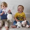 Two young children are sitting on the floor playing with stuffed toys. Produktbild-Vorschau