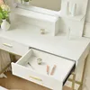A close-up view of a white vanity table with gold accents, showing an open drawer with makeup items inside. Produktbild-Vorschau