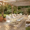 An outdoor patio setting with a wooden pergola, a table set for dining, and surrounding garden. Produktbild-Vorschau