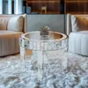 A mirrored round coffee table with a small plant on top, placed on a fluffy white rug in a living room setting with sofas in the background. Anteprima dell’immagine prodotto