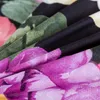 A close-up of a floral patterned fabric, likely bedding, showing folded layers of material with large, vibrant flowers in shades of purple, pink, and green against a black background. Produktbild-Vorschau
