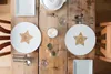 A table setting for two on a wooden table with white plates featuring a wooden star design. Produktbild-Vorschau