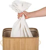 A hand is holding a white laundry bag over a bamboo laundry basket. Voir les images du produit