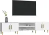 A white TV stand with wooden legs and handles, with a flat-screen TV mounted on the wall above it. A vase with greenery is on the left side of the stand. Náhľad obrázku produktu