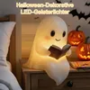 A cute ghost lamp reading a book sits on a nightstand next to two jack-o'-lanterns. Produktbild-Vorschau