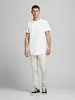 A man is standing in front of a plain background wearing a white t-shirt and light-colored pants. Produktbild-Vorschau
