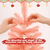 Hands adjusting the branches of a pink artificial Christmas tree, with festive decorations at the top and text overlay. Anteprima dell’immagine prodotto