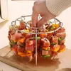 A hand is shown placing skewers into a circular grill rack filled with meat and vegetables. Náhľad obrázku produktu