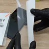 Hands wearing black gloves are applying a screen protector to a smartphone. Produktbild-Vorschau