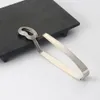 A stainless steel escargot tong rests on a black serving dish. Produktbild-Vorschau