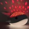 A whale-shaped night light projecting stars onto a wall. Produktbild-Vorschau