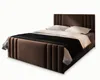 A brown upholstered bed with white pillows and a black blanket, presented on a white background. Produktbild-Vorschau