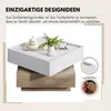 A white square coffee table with a wood-toned base, decorated with a small vase and a lidded jar. Produktbild-Vorschau