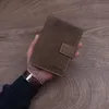 A hand holding a brown leather wallet on a wooden surface. Produktbild-Vorschau