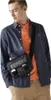 A man wearing a blue shirt and orange polo shirt, with a black messenger bag. Anteprima dell’immagine prodotto