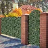 A garden fence covered in artificial ivy with a brick gate and house in the background. Voir les images du produit